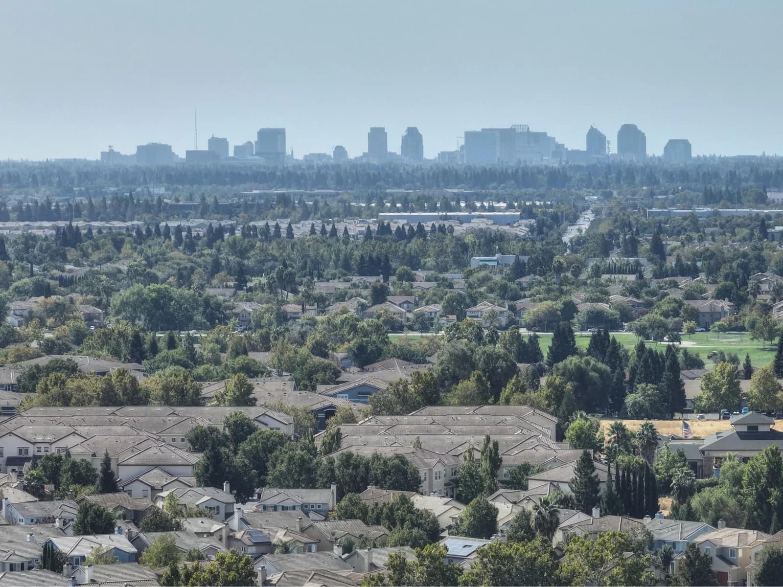 Aerial view of Sacramento's suburban homes with the city skyline in the distance. Lush greenery and clear skies.