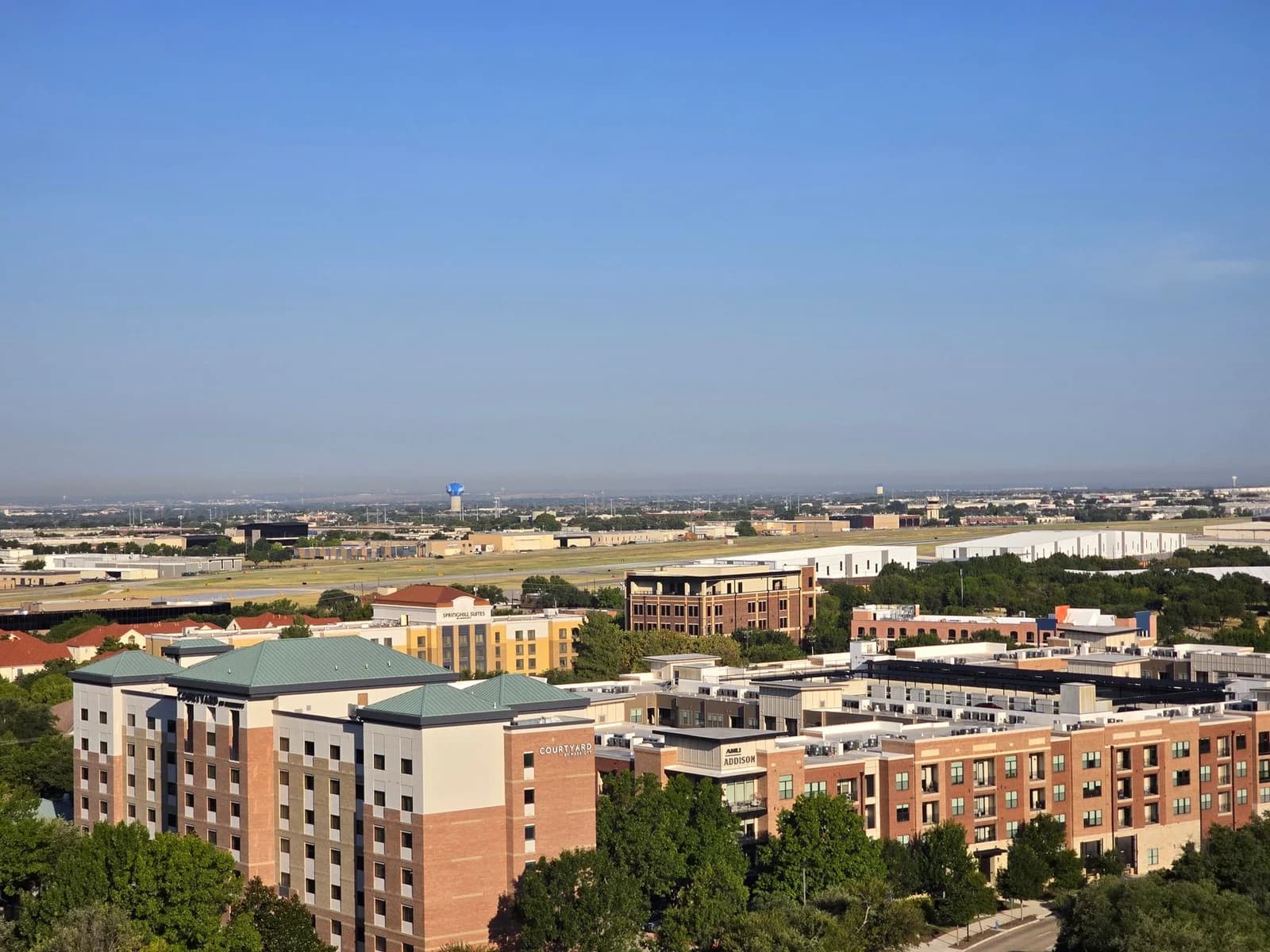 Aerial view of a cityscape with buildings and open spaces under a clear blue sky.