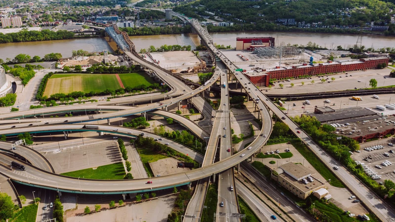 Drone view of modern cars riding through junction above greenery and broad river