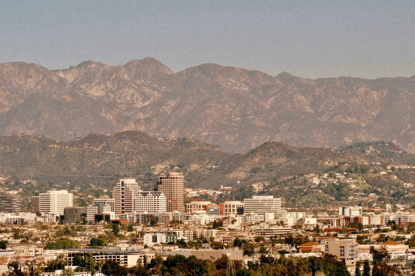 Aerial view of a city skyline with mountains in the background under clear skies.