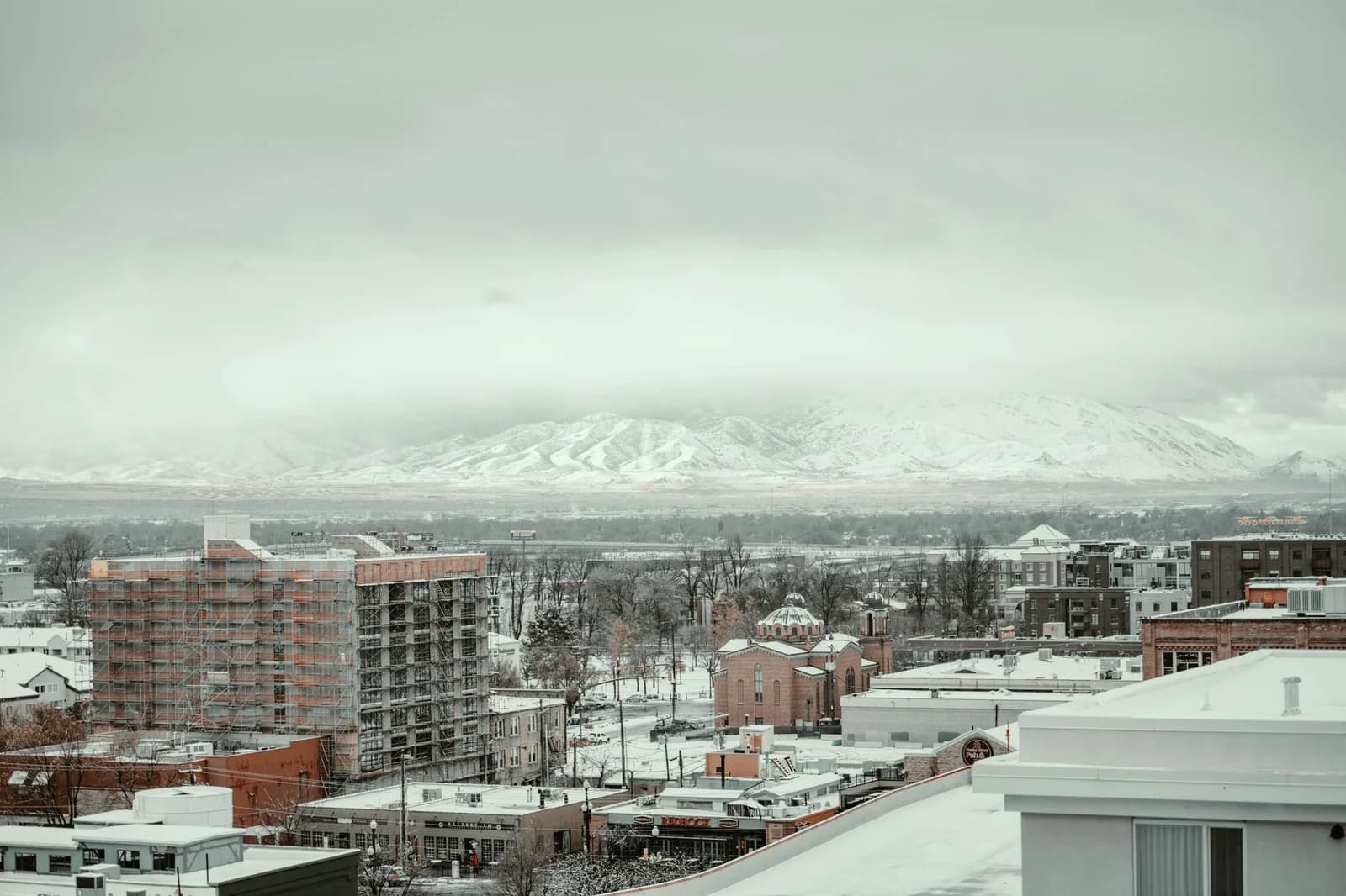 A winter cityscape view in Salt Lake City with snow-covered buildings and mountains in the background.