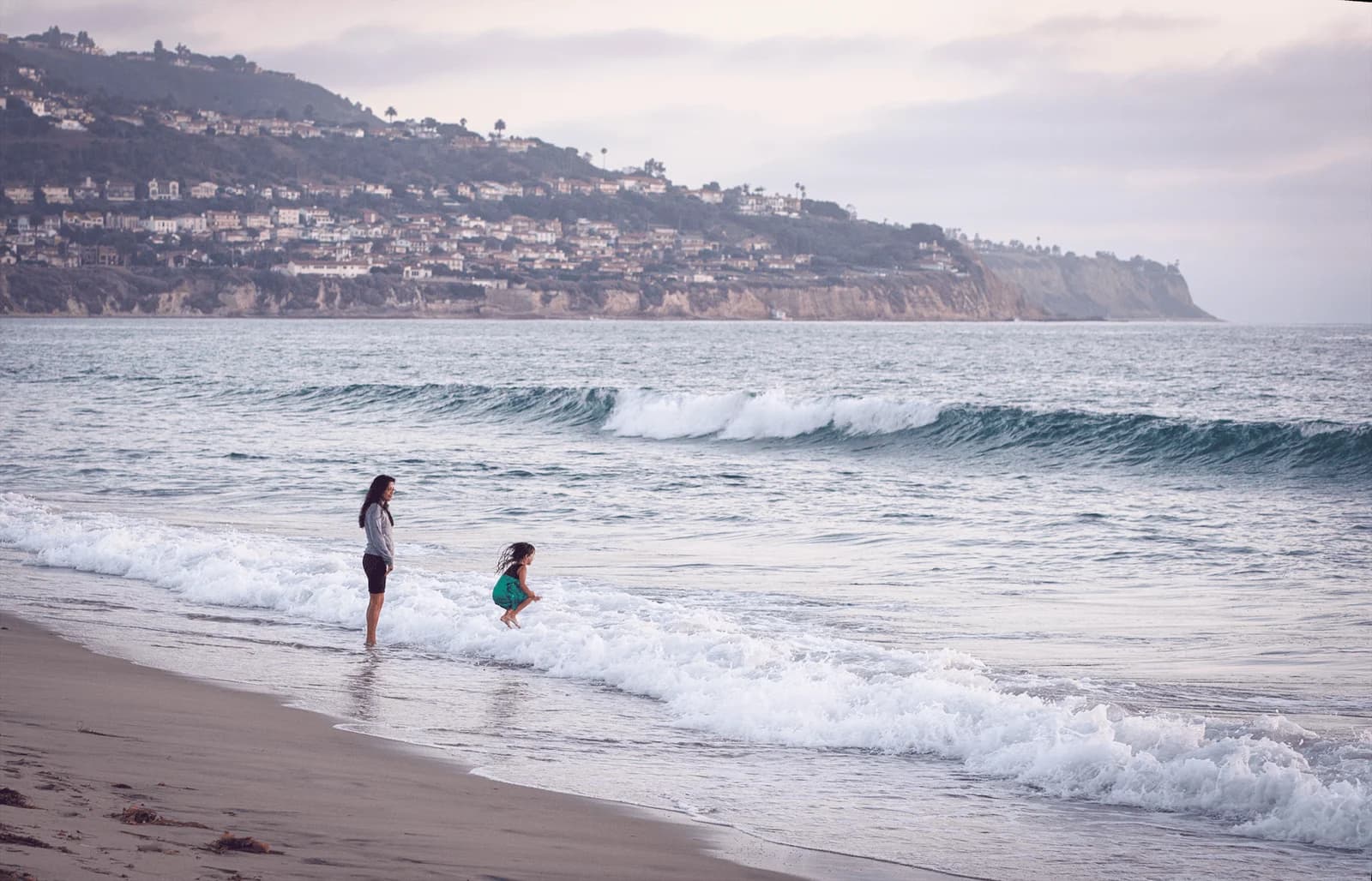 Mother and daughter joyfully playing by the waves at Redondo Beach, California.