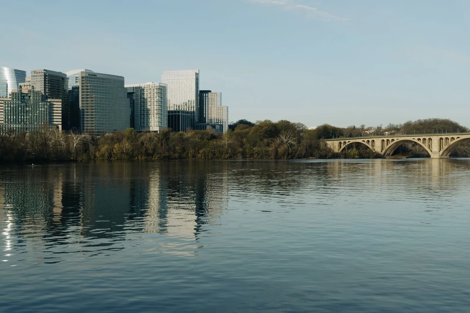 A scenic view of skyline buildings and Key Bridge reflecting on the Potomac River.